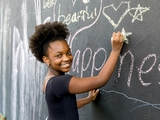 Young teen coloring at an outdoor chalk wall.