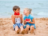 Two kids on the beach eating watermelon