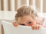 Shy girl hiding her face behind a chair