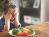 Young girl with hands over eyes sitting in front of a plate of food