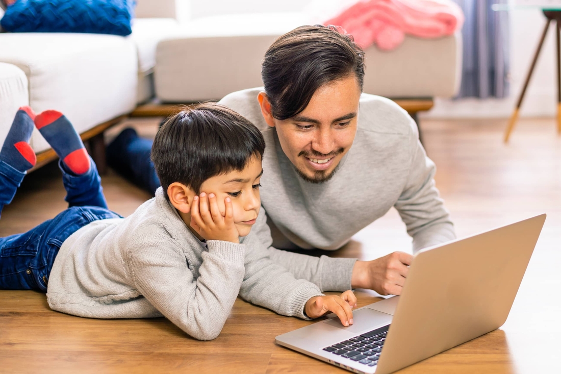 Father and son smiling together looking at a laptop computer.