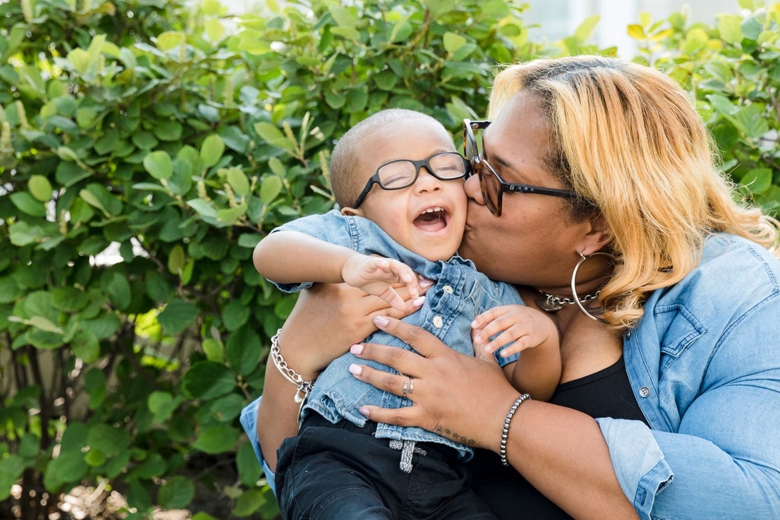 African american mom kissing her smiling baby boy in the hospital garden