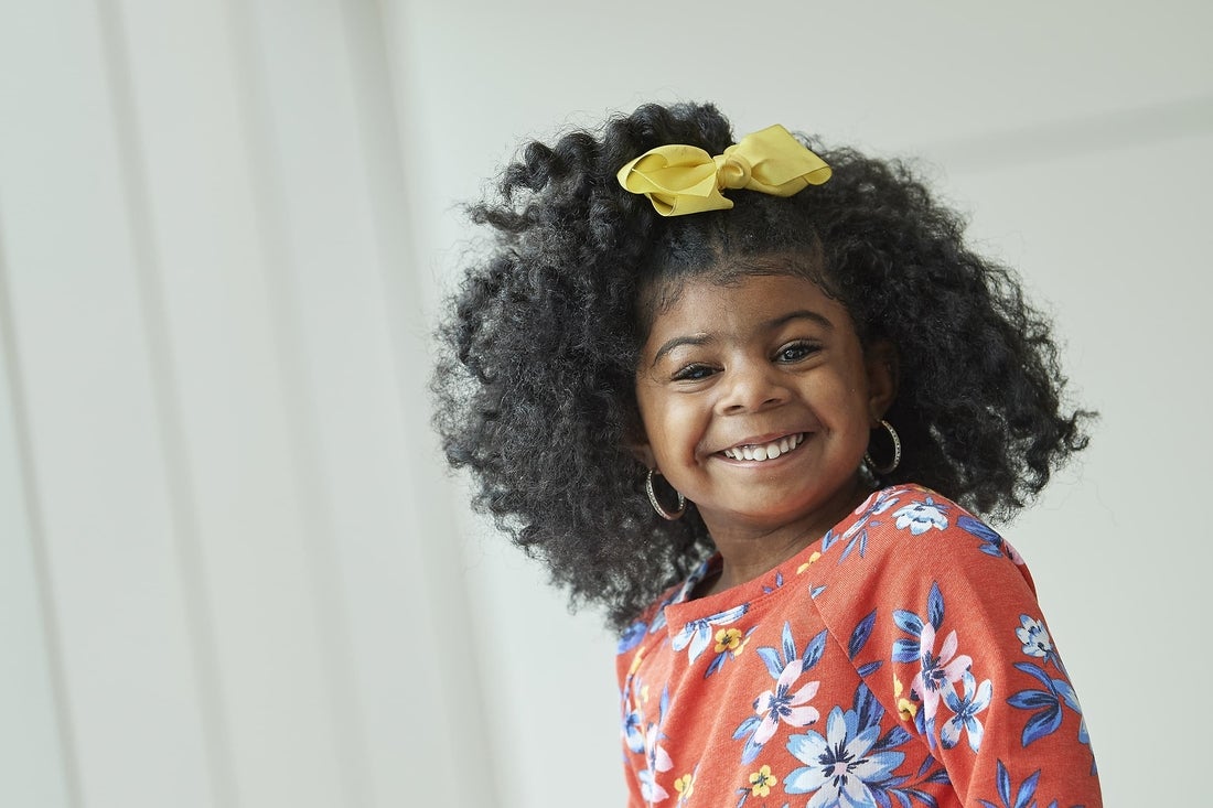 Smiling african american girl wearing a dress with flowers and a yellow bow on her hair