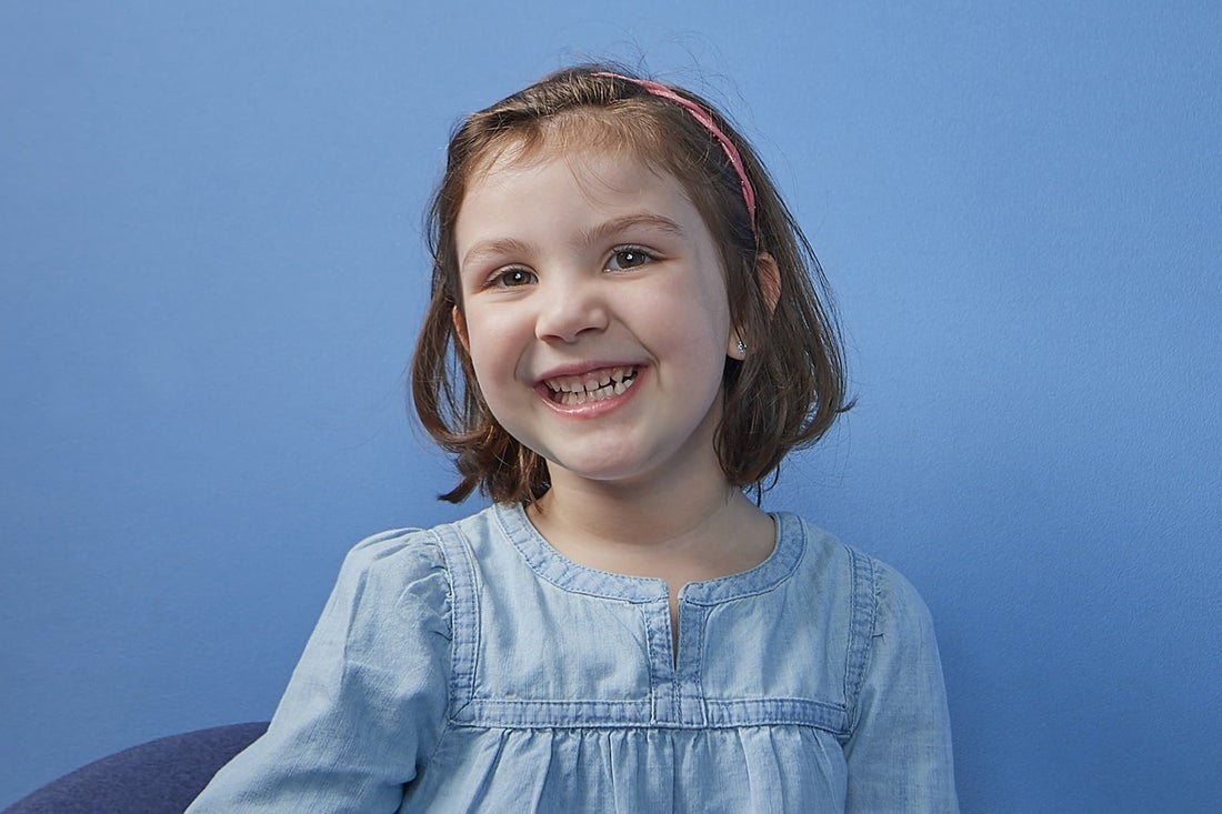 Smiling young girl wearing a light blue dress and a pink headband.