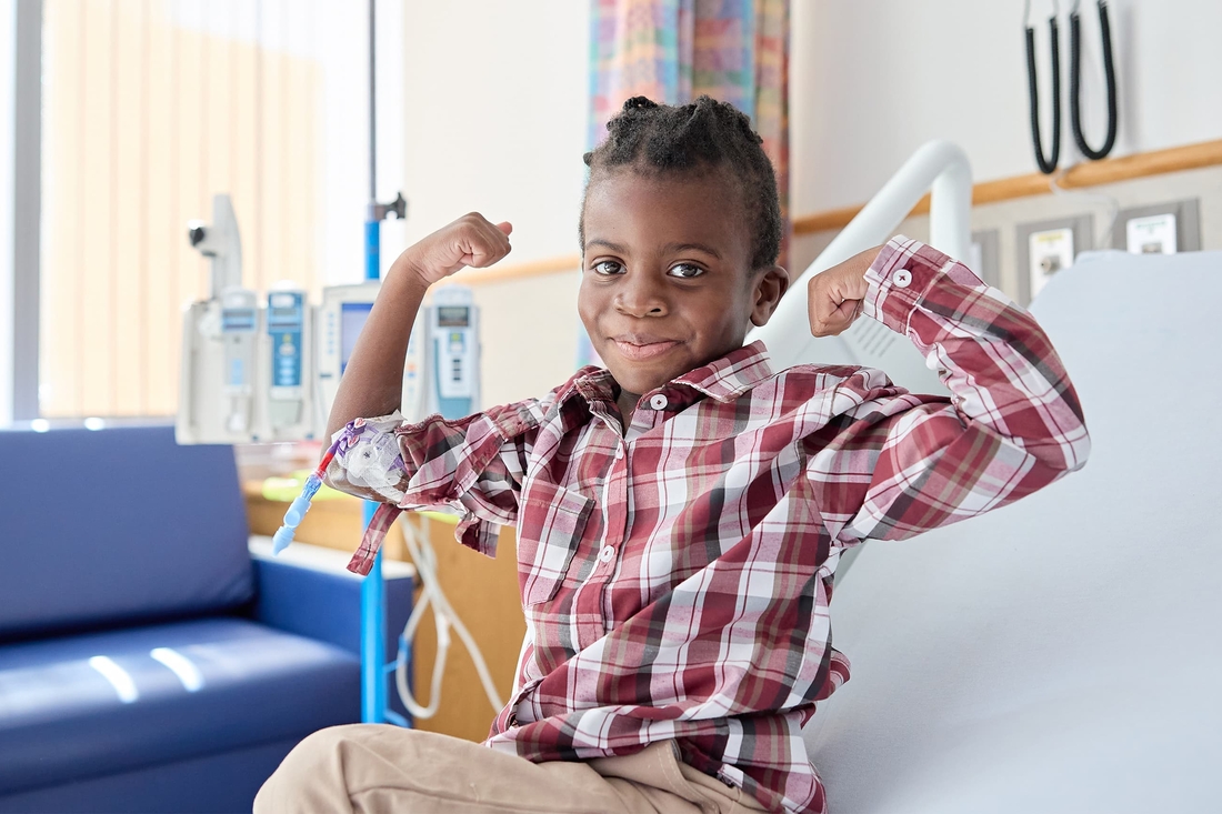 boy showing his muscle and smiling while he sits on the hospital bed.