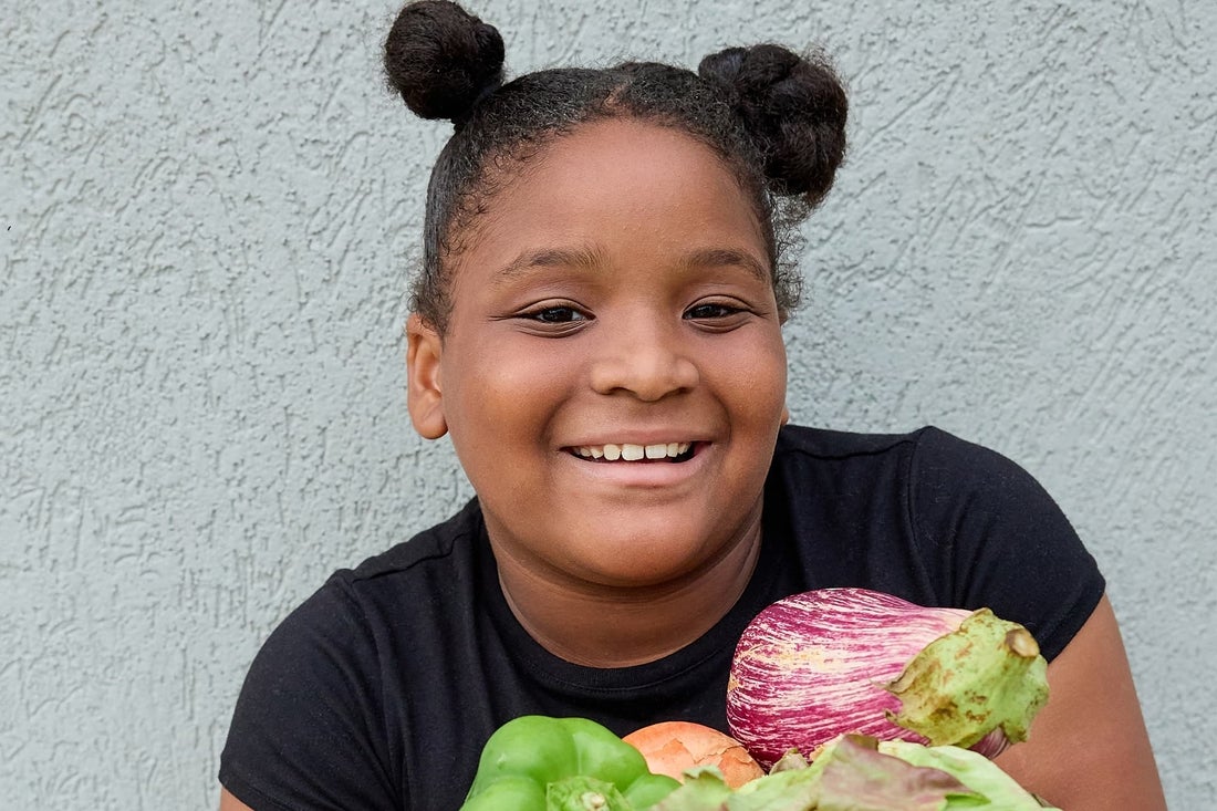 young girl smiling and holding vegetables.