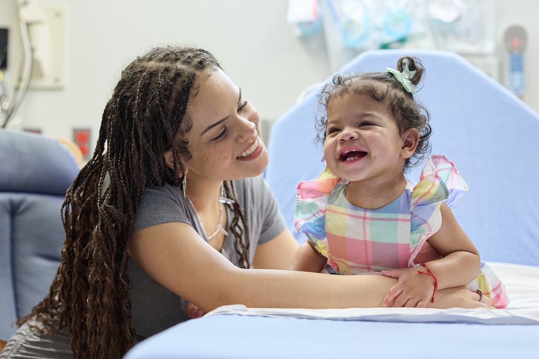 baby girl wearing a colorful dress and laughing with her mother.