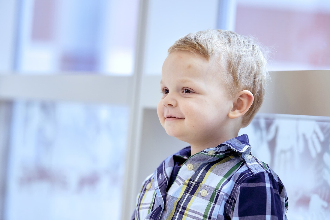 Blonde young boy smiling and wearing a checkered shirt.