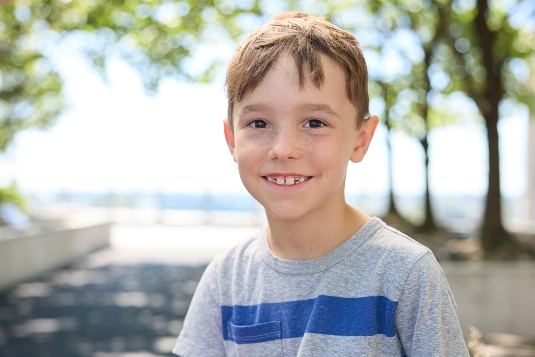 Freckled boy with striped grey t-shirt smiling in the hospital garden.