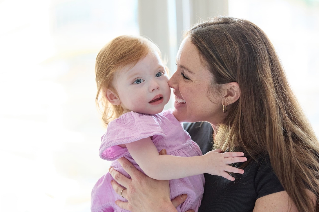 mother smiling at her redhead baby girl with blue eyes and a pink dress.