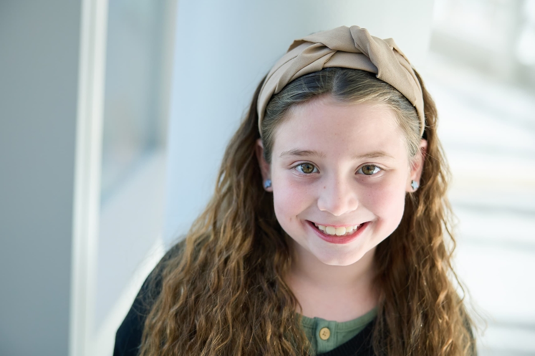 Young girl with beige headband and curly hair smiling at the camera.