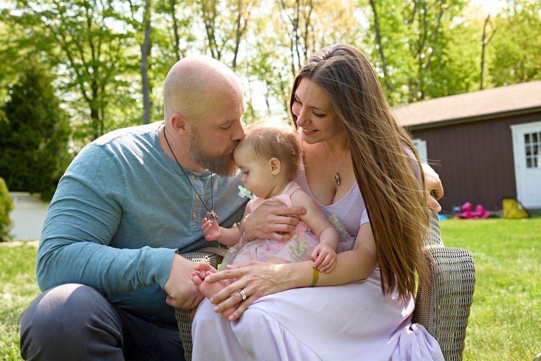 Beautiful family outside with Father, Mother, and baby looking at necklace containing  ashes of her sister.