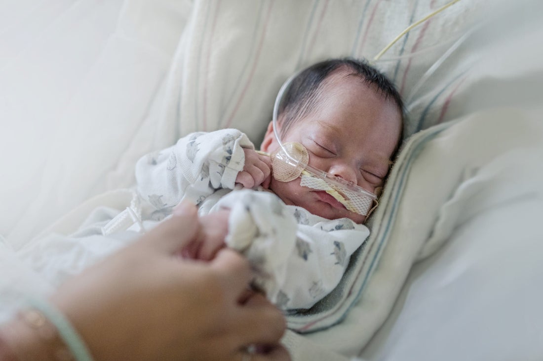 Mom holding hand of a newborn intensive care baby