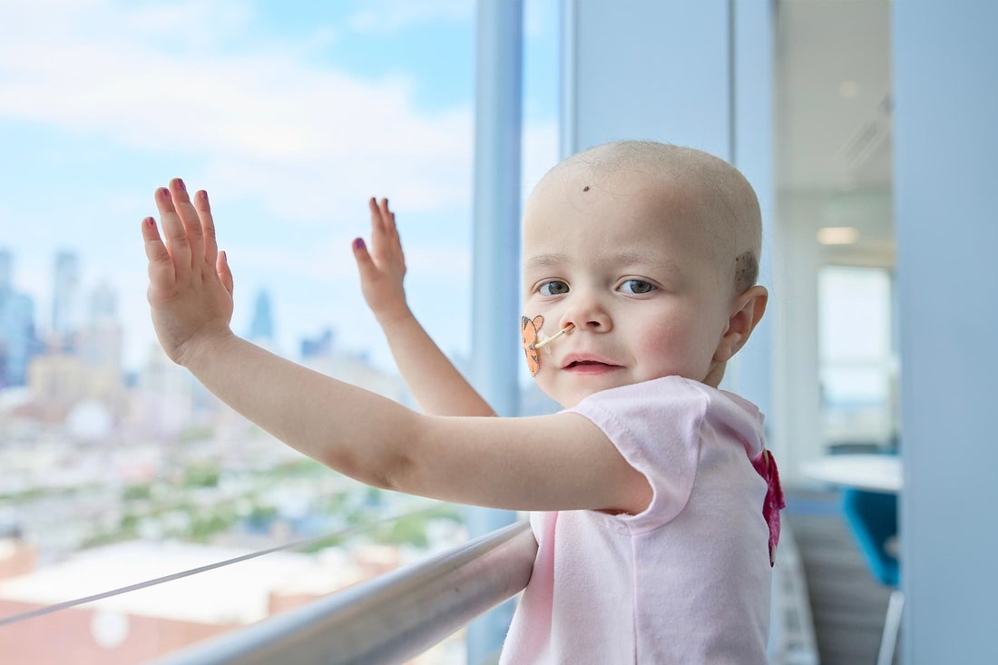 Little girl bald with cancer looks hopeful and happy at viewer.