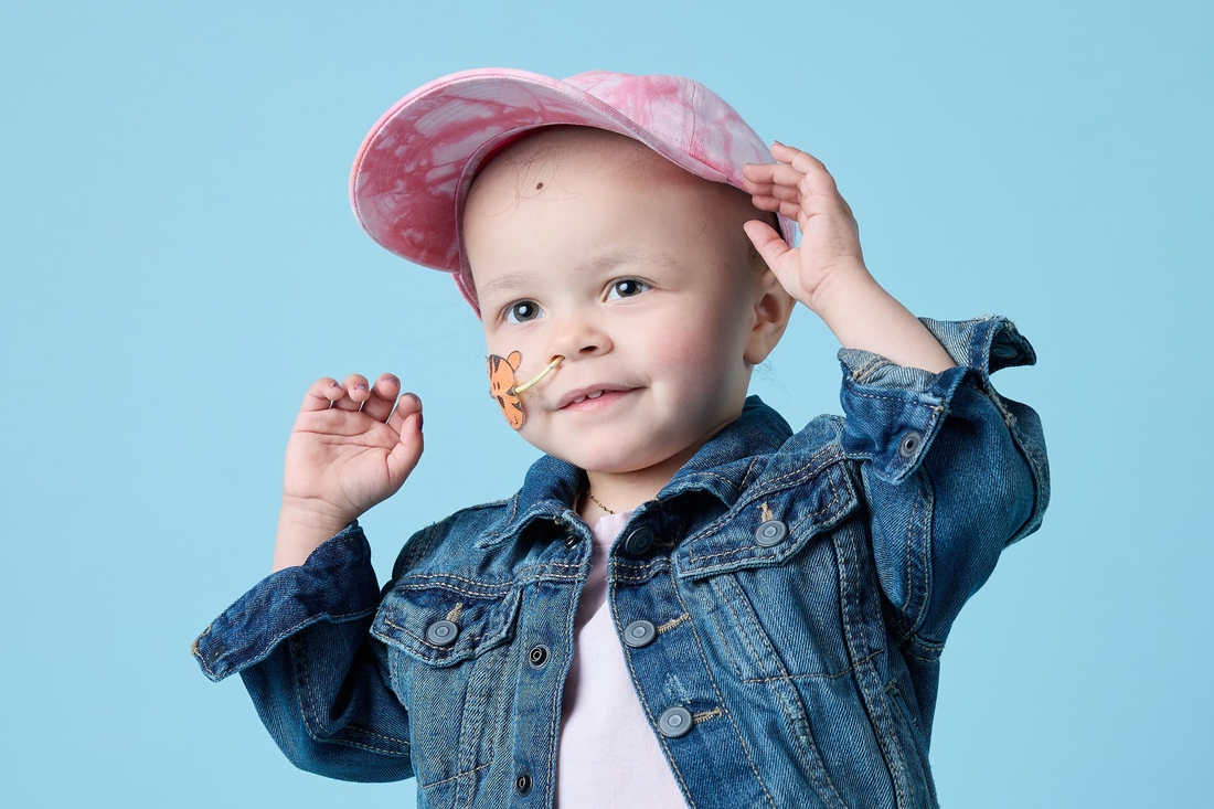 Adorable young child cancer survivor with jean jacket and cap.