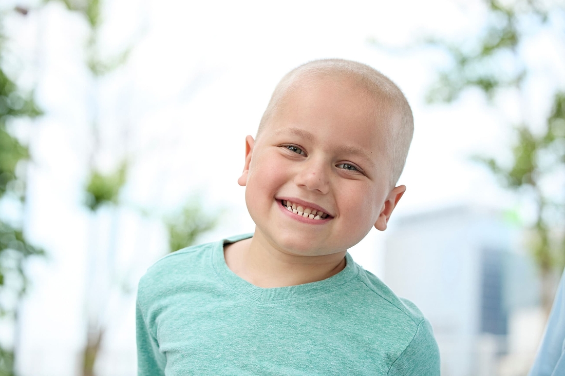 Cancer survivor tween aged child smiling ouside in a courtyard.