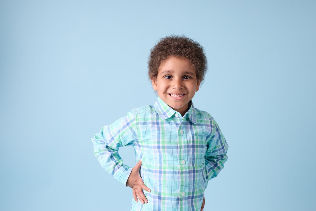 A young smiling boy, who is also a leukemia patient, is wearing plaid shirt on blue background.