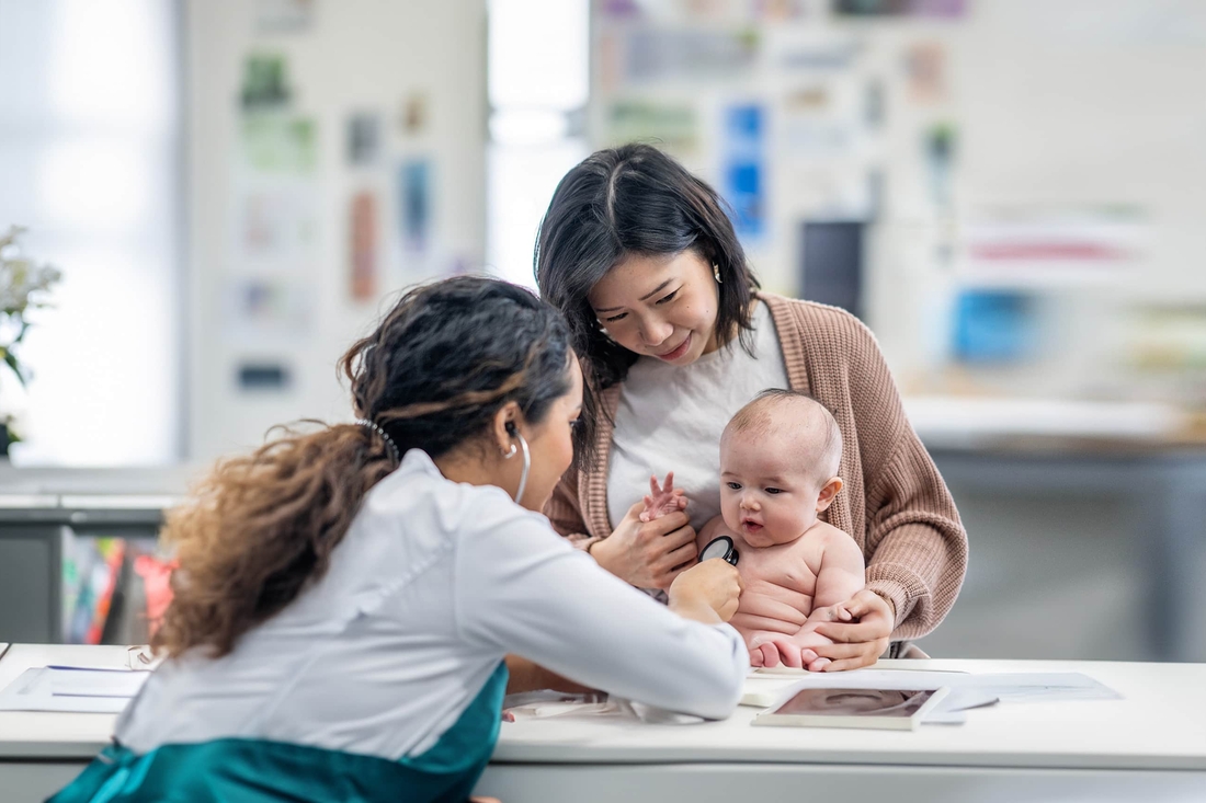 Mother holding her baby as physician performs examination