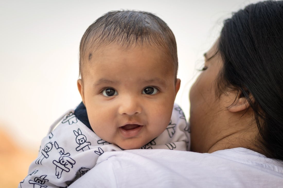 Baby looking ahead being held by her up by her mother. 