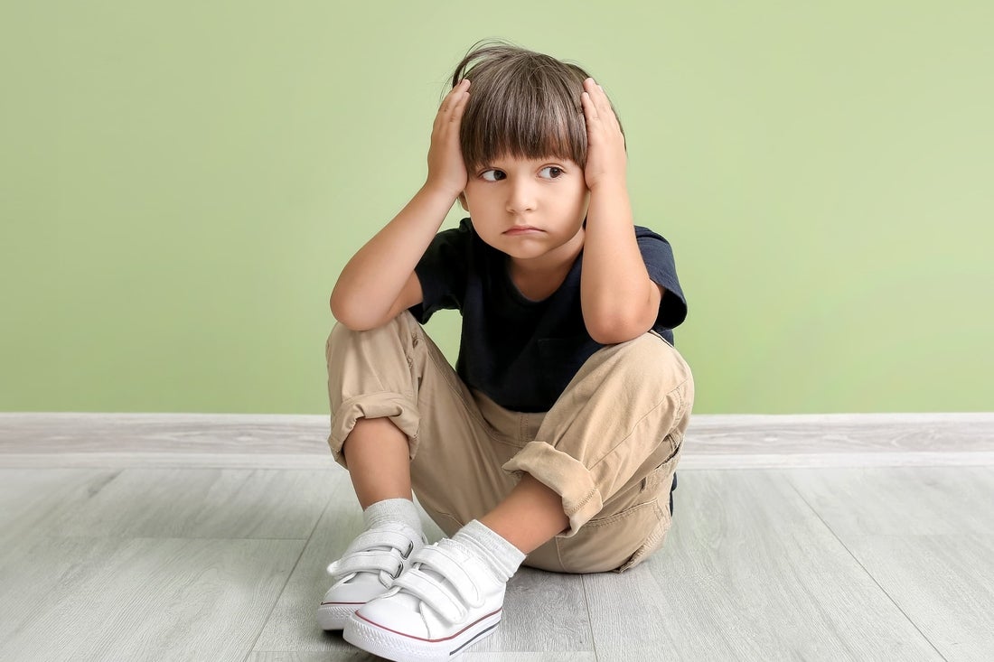 School-age boy sitting on ground with headache with green background.