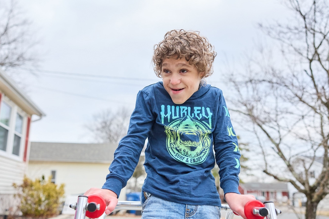 A curly-haired boy with a neurological condition using crutches to assist with walking.