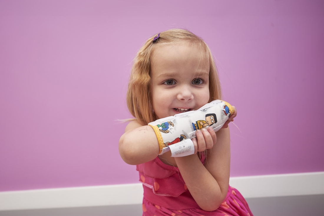 Young girl smiling holding her arm thats in a brace against a purple wall.