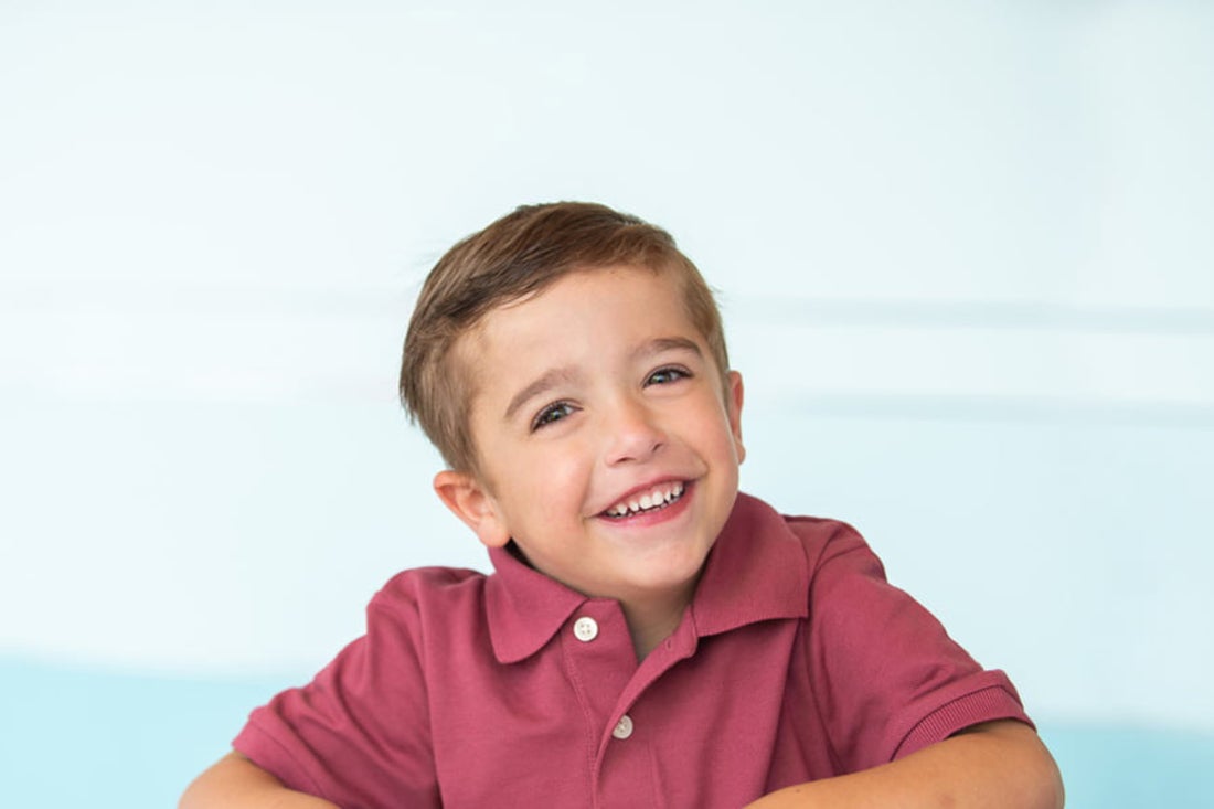 Little boy wearing red polo smiles at camera.