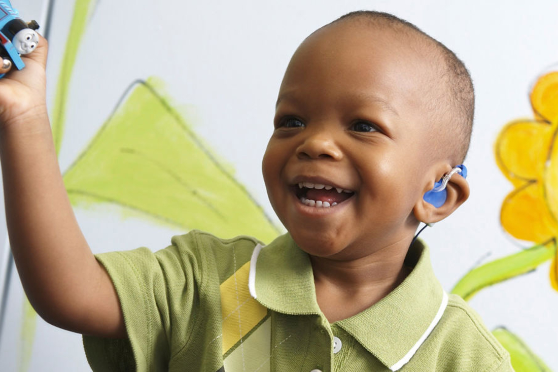 Smiling little boy wearing a green polo and hearing aids.