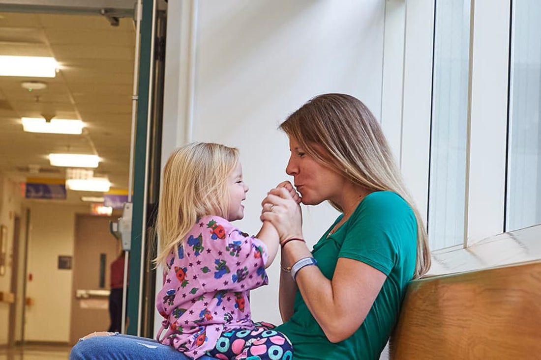 Mother sitting in hospital hallway, playing with daughter sitting on her lap