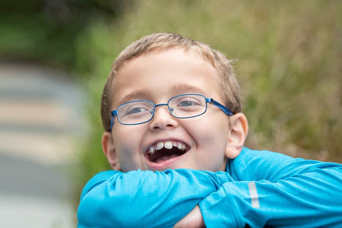 Young boy with glasses and blue shirt smiling at the camera.