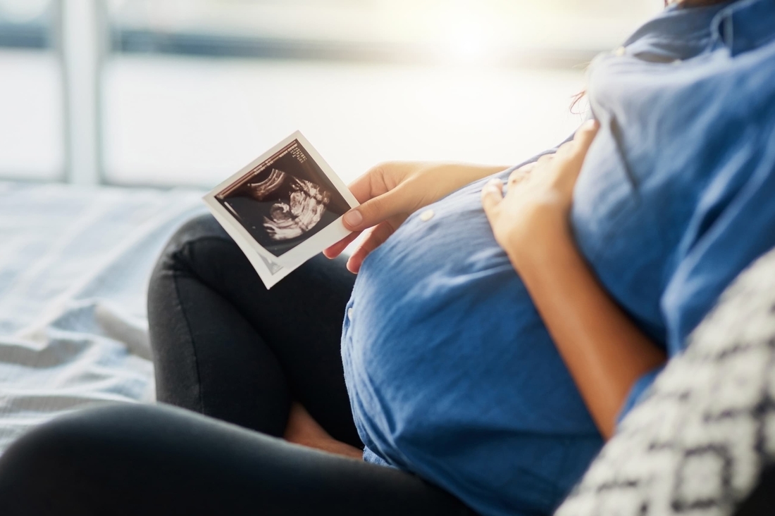 Pregnant woman looking at a sonogram with her hand resting on her abdomen