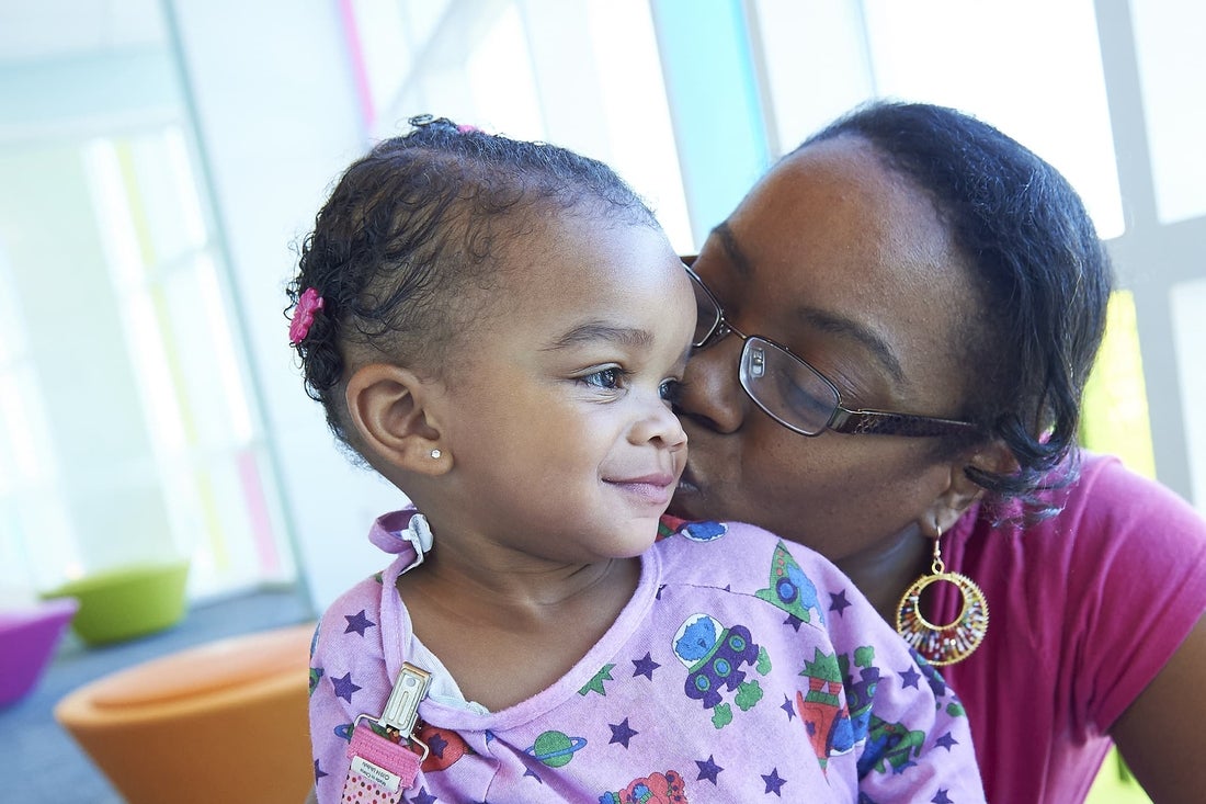 Mother kissing cheek of daughter in hospital gown