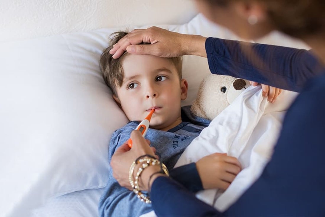 Young child in sick in bed having temperature taken.