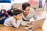 Father and son smiling together looking at a laptop computer.