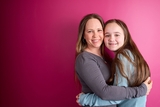 Happy teenage girl with long hair hugging her mother on a magenta pink background