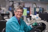 Lab worker sitting at microscope and smiling