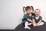 Happy little girl with pigtails sitting with her infant sibling on a grey round chair 