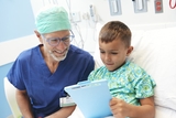 Blonde boy in hospital bed showing a game to his pediatrician