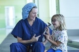 Female doctor and blonde girl smiling while holding an otoscope