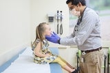 Pediatrician examining smiling little girl with yellow dress