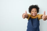 Boy smiling and doing a thumbs-up with both hands.