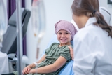 An elementary age girl talking to medical doctor wearing headscarf receiving infusion.