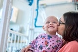 Little girl with cancer in hospital getting kiss on cheek from her mom.