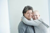 Teen girl cancer survivor with her mother on plain wall.