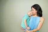 Child with cancer in mint green tshirt being held in arms by her mother.