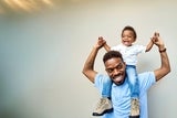 Little boy laughing while sitting on his dads shoulders.