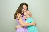 Older sister in purple dress hugging and offering support to her younger sister who is a cancer survivor.