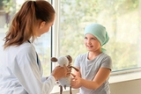 Cancer patient interacting with woman doctor who is handing her a stuffed animal.