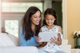 Mom and daughter smiling and looking at the tablet.