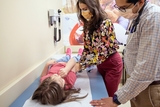 Nurse examining a young female patient in a hospital bed while the doctor observes.